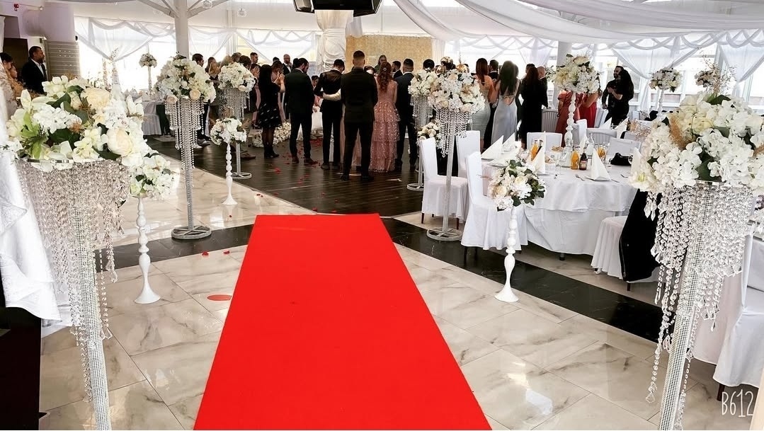 Höga blomsterpelare i vitt och crème med eleganta kristalldetaljer. Mjukt draperade tak, stilrena stolsuppsättningar och en vackert dekorerad fond