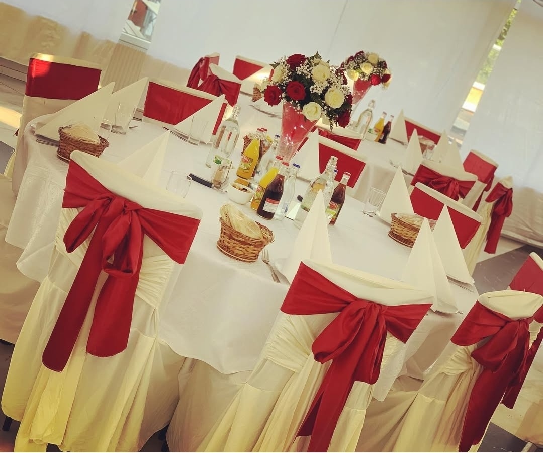 Stilfull bröllopsdukning i klassiskt vitt med djup­röda sidenrosetter, blomsterarrangemang i rött, crème och grönt ger rummet karaktär och värme.