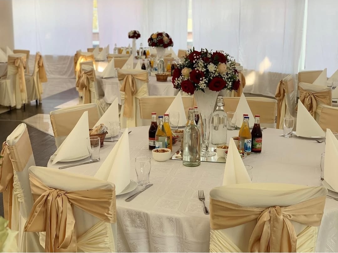 Elegant bröllopsdukning i vitt och champagne med runda bord med vinröda detaljer