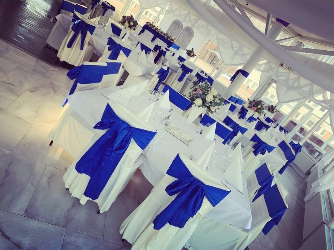 Stilren dukning i vitt och djup kungligt blått skapar en elegant och tidlös känsla. Mjukt klädda stolar med rosetter och prydligt vikta servetter.