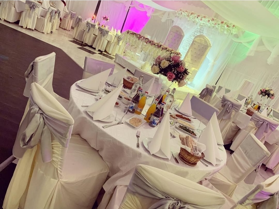 Elegant bröllopsdukning i sofistikerade silver- och vittoner. Bord med vita dukar, stilrena stolsöverdrag med silverfärgade rosetter och noggrant utvalda detaljer.